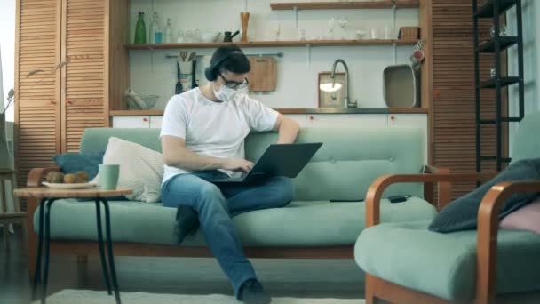 Mężczyzna w izolatce obsługuje laptopa w salonie. Mężczyzna pracuje w domu w czasie kwarantanny podczas epidemii Kowid-19. — Wideo stockowe