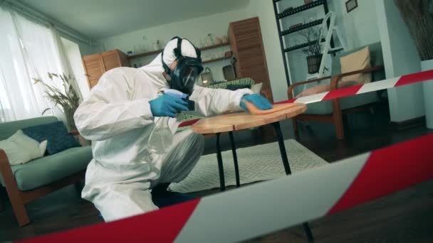 Eine Person im Schutzanzug putzt einen Tisch in einer Wohnung. Desinfektionsprozess bei Covid-19-Pandemie. — Stockvideo