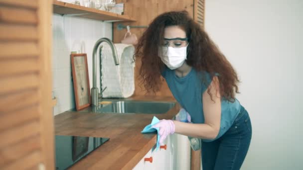 Une femme portant un masque facial utilise un désinfectant pour nettoyer la table. Coronavirus, concept de prévention COVID-19 . — Video