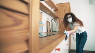 Güzel bayan maske takarken masa yüzeyini dezenfekte ediyor.
