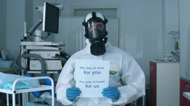 Trabajador de la clínica en traje protector insta a la gente a quedarse en casa . — Vídeos de Stock