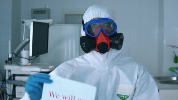 Egy vegyvédelmi ruhás ember mutat egy posztert, aki éljenzi az embereket a világjárvány idején.. — Stock videók