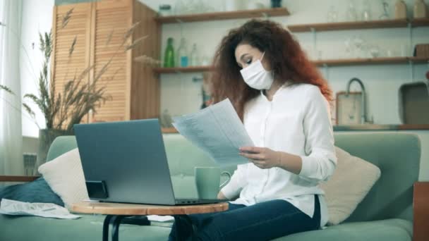 Werk vanuit huis tijdens de covid-19 pandemie. Een vrouw met een gezichtsmasker werkt thuis in quarantaine. — Stockvideo