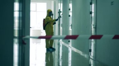 Su sıçratma kıyafeti giymiş müfettiş koridoru sterilize ediyor. Coronavirus salgını, virüs önleme, COVID-19 konsepti.