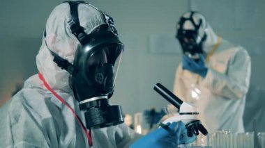 Koruyucu giysili bir adam salgın sırasında laboratuarda test tüpleriyle çalışır..