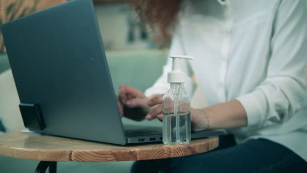A nő fertőtleníti a kezét, miközben otthon gépel egy laptopon.. — Stock videók
