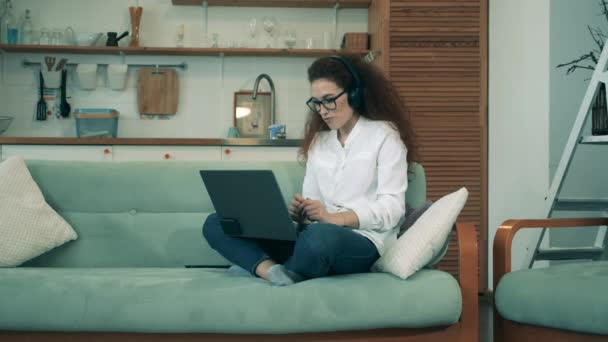 Ung kvinna i hörlurar via laptop under karantänen. Distansutbildning, distansundervisning. — Stockvideo