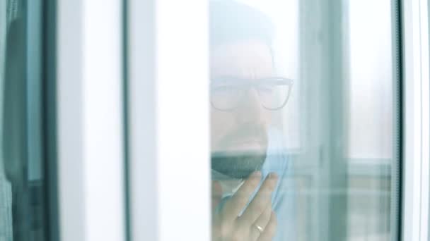 L'uomo indossa una maschera mentre guarda la finestra durante la quarantena . — Video Stock