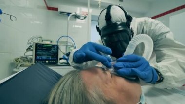 Coronavirus COVID-19 konsepti. Tehlikeli madde giysisi içinde bir sağlık görevlisi bir hastaya oksijen maskesi takıyor.