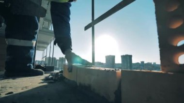 İşçi çok katlı bir binanın tepesine tuğla örüyor.