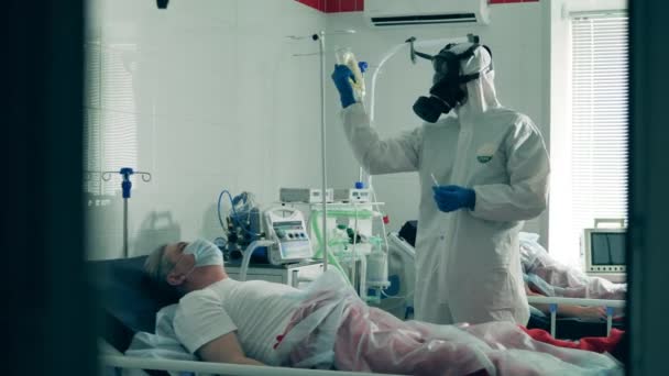 Coronavirus, patient med covid 19 på intensivvårdsavdelningen på ett sjukhus. Doktorn i plaskdräkt ger dropp. till en äldre patient — Stockvideo