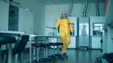 Sarı hazmat odasındaki bir adam odayı dezenfekte ediyor..