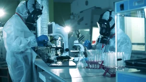 Forskare i skyddsdräkter arbetar med mikroskop under en pandemi. — Stockvideo