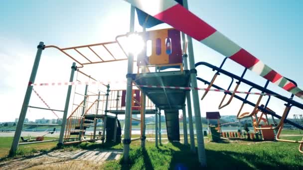 Parque infantil vazio durante a pandemia do coronavírus. Fita de barricada em um playground iluminado pelo sol sem ninguém nele — Vídeo de Stock