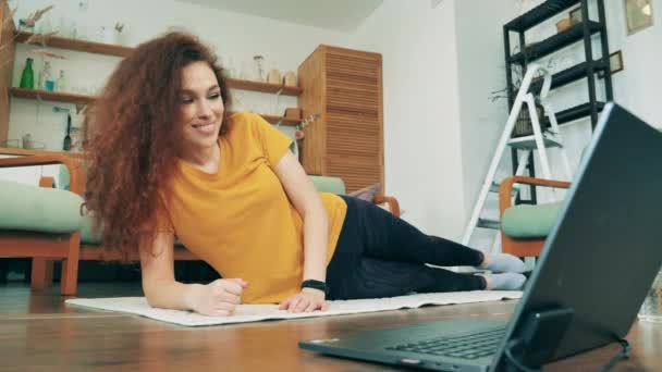Mulher sorridente se exercita em um tapete em casa durante a quarentena. Conceito de aprendizagem remota . — Vídeo de Stock