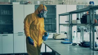 Tehlikeli madde giysisi giymiş bir adam kimya laboratuvarında bir masayı temizliyor.