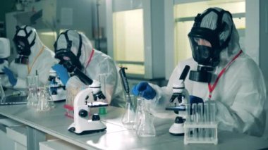 Tehlikeli madde giysileri içindeki işçiler mikroskop altında sondaları inceliyorlar..