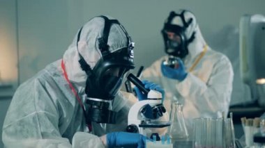 Tehlikeli madde giysisi uzmanı analiz sırasında mikroskop kullanıyor. COVID-19 Laboratuvarı, Coronavirüs antikor araştırma konsepti