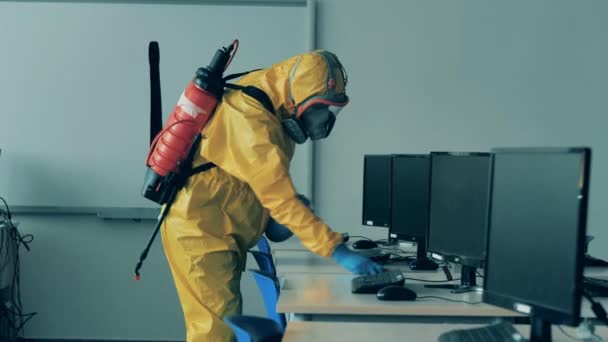 Een man in een hazmat pak desinfecteert een computerklas. — Stockvideo