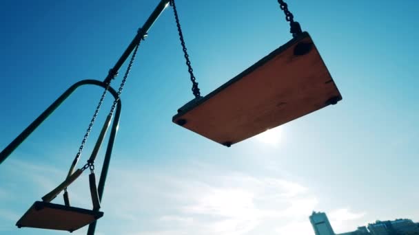 Sunlit playground swings swaying with nobody on them — Stock Video