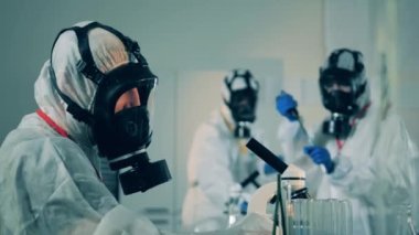 Tehlikeli madde giysisi içindeki laboratuvar çalışanı COVID-19 sırasında mikroskop kullanıyor. Coronavirüs antikor araştırması..