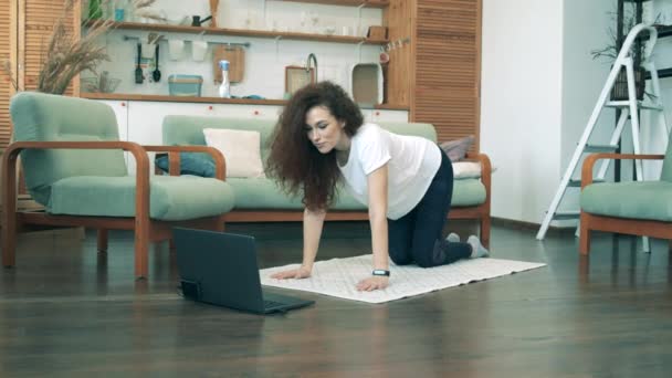 Bella dama está haciendo deportes con su portátil en casa. COVID-19 concepto de bloqueo . — Vídeo de stock