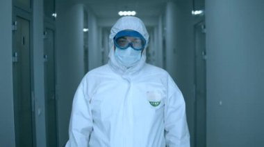 Bir doktor kameraya bakıyor, koruyucu gözlük takıyor..