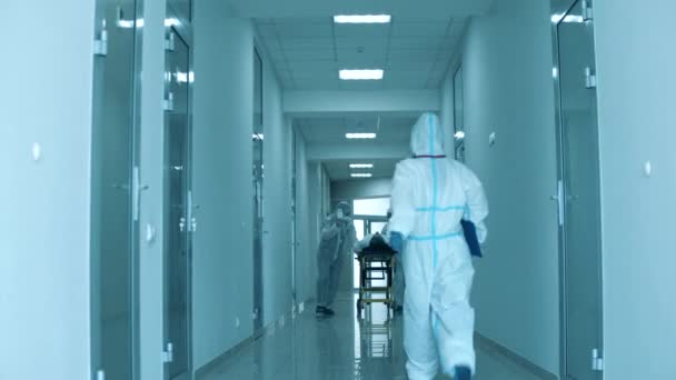 Médicos en materiales peligrosos trasladan al paciente en camilla a una habitación de hospital . — Vídeos de Stock
