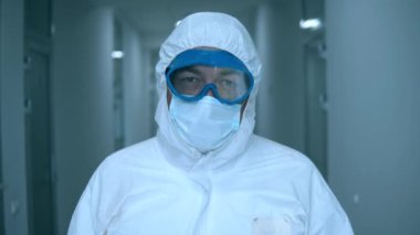 Tehlikeli madde uzmanı klinik koridorunda dikilirken kameraya bakıyor..