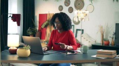 Afro-Amerikalı bayan evden alışveriş yapmak için laptop ve kart kullanıyor. Çevrimiçi alışveriş kokteyle.