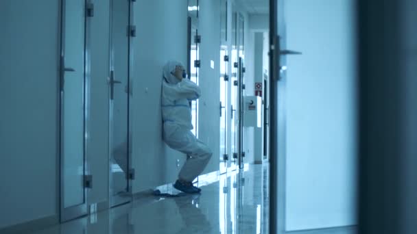Kvinnlig läkare glider ner på väggen och tar av sig sin utrustning — Stockvideo