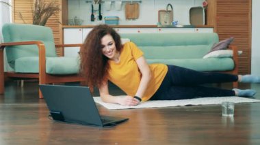 Kilitleme konsepti, koronavirüs salgını. Bir bayan yerde yatarken egzersiz yapıyor ve gülümsüyor.