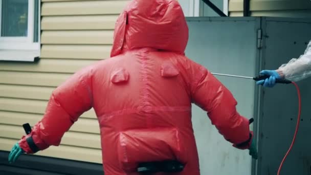 Desinfectante químico está siendo rociado sobre un trabajador en un traje rojo — Vídeos de Stock