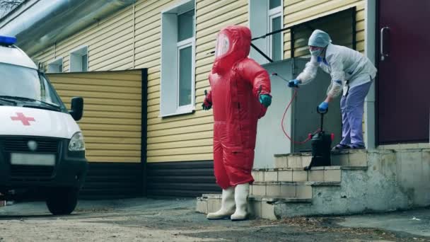 Paramedic in a red suit is getting disinfected by a nurse — Stock Video