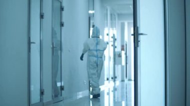 Tehlikeli madde giysisi içindeki doktor koridorda dinleniyor.