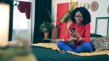 Genç Afrikalı kadın elinde telefon ve kartla alışveriş yapıyor.