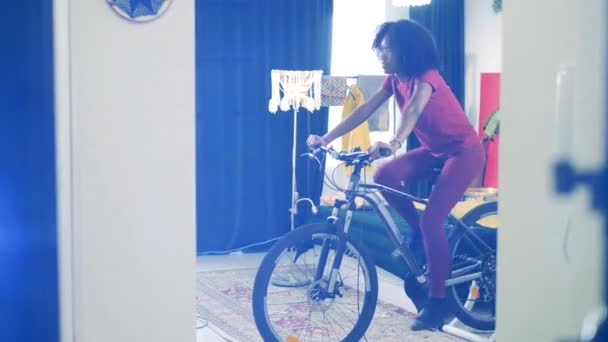 Afrikansk kvinna har en cykelträning hemma. Sport hemma, fitness hemma koncept. — Stockvideo