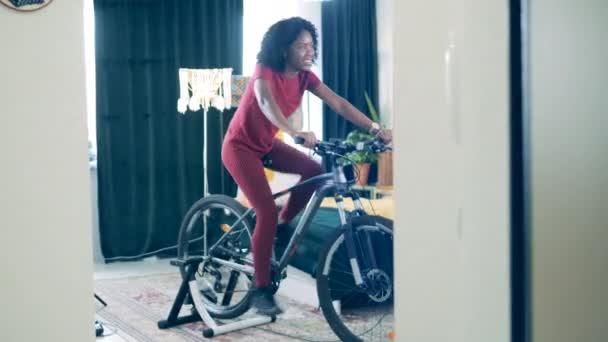 Joven dama africana está utilizando una máquina de ciclismo para entrenar en casa — Vídeo de stock
