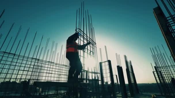 Trabajador de la construcción teje barras en la carcasa sobre un fondo atardecer . — Vídeo de stock