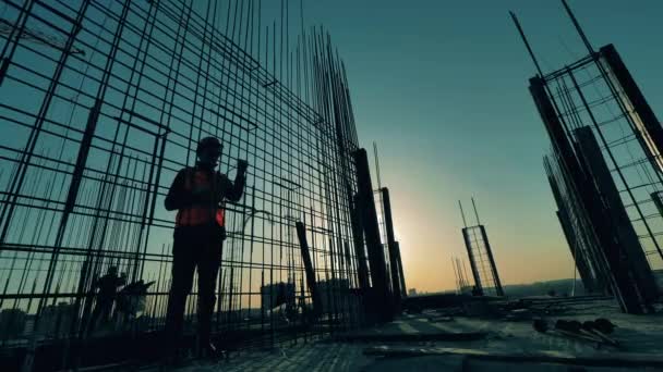 Man bouwer breit metalen karkas op zonsondergang achtergrond. — Stockvideo