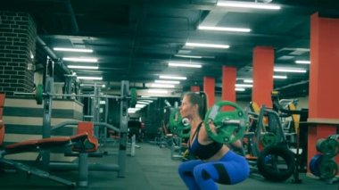 Bir sporcu kavis yaparken halterle çömeliyor..