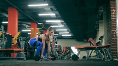 Bir kadın spor salonunda antrenman yaparken küçük bir halteri kaldırır..