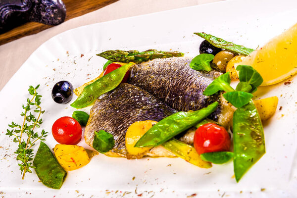 Fillet of Dorado fish baked with vegetables on white plate