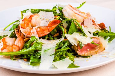 Roket salata karides ile ton balığı ve parmesan peyniri beyaz plaka üzerinde