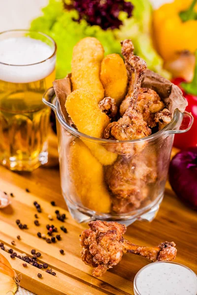 Fish fingers and fried chicken in glass bowl served with beer