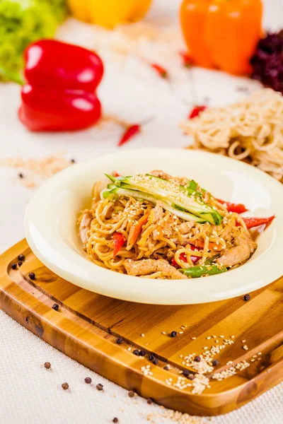 Noodles with vegetables and chicken in beige plate on wooden board