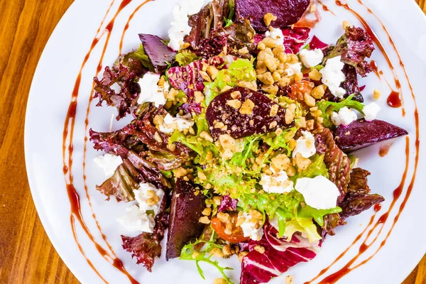 Pişmiş kırmızı pancar, keçi peyniri, ceviz, domates ve beyaz plaka üzerinde otlar ile karışık salata. Üstten Görünüm