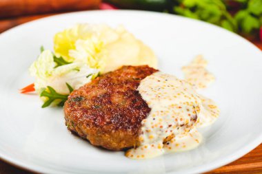 Beyaz tabakta yeşil salatayla servis edilen hardal soslu et pirzolası..