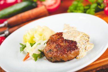 Beyaz tabakta yeşil salatayla servis edilen hardal soslu et pirzolası..