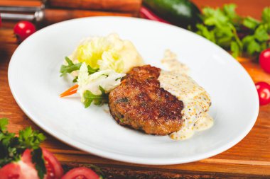 Beyaz tabakta yeşil salatayla servis edilen hardal soslu et pirzolası..
